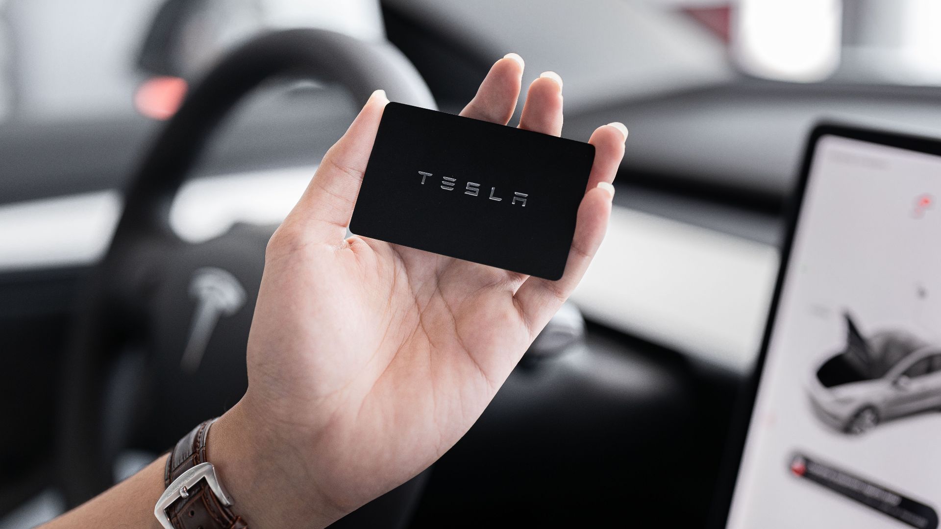 Close-up of a hand holding a key card inside a modern car interior with digital display.