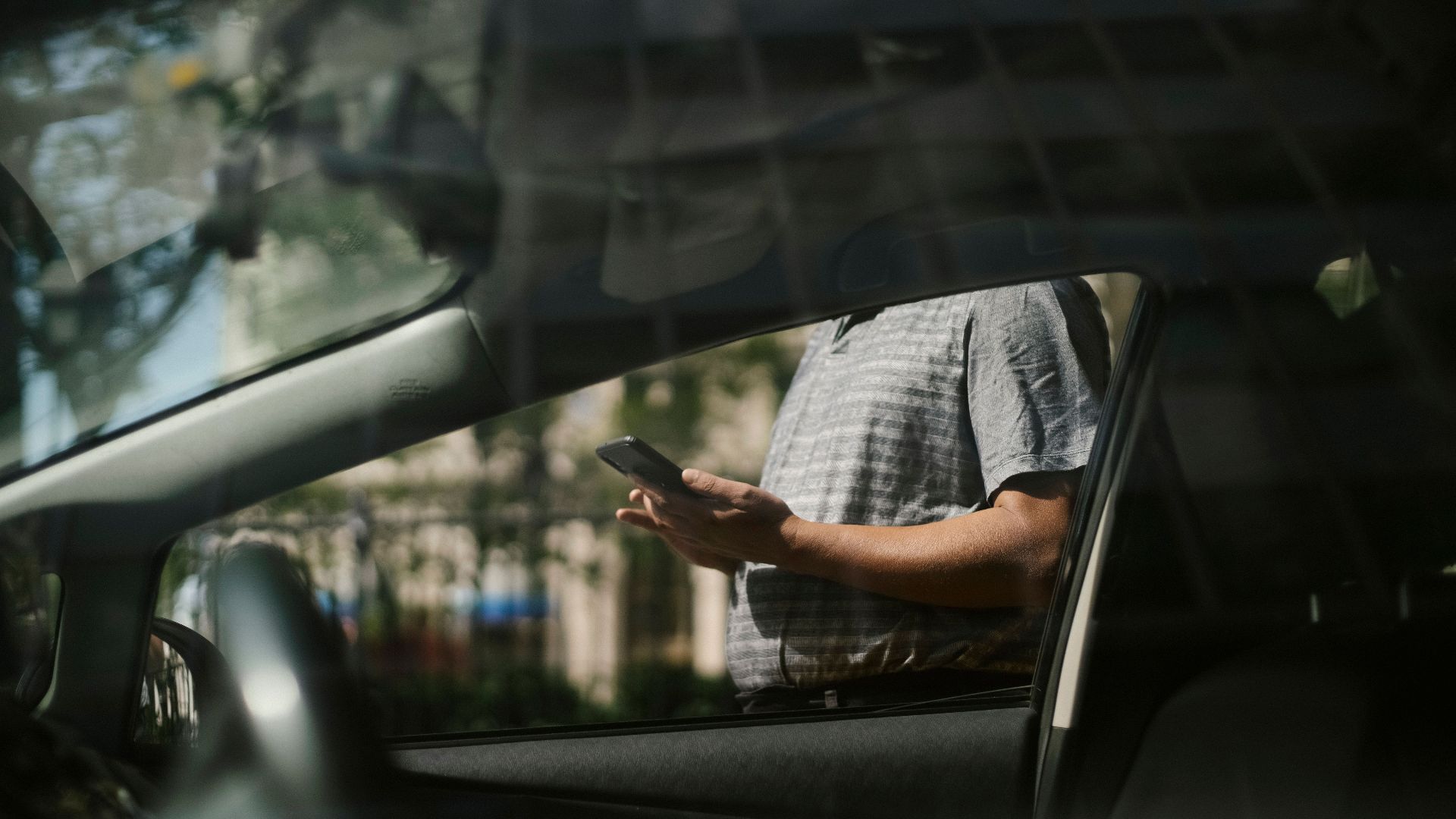 Through glass side view of crop anonymous male browsing mobile phone while standing near cab