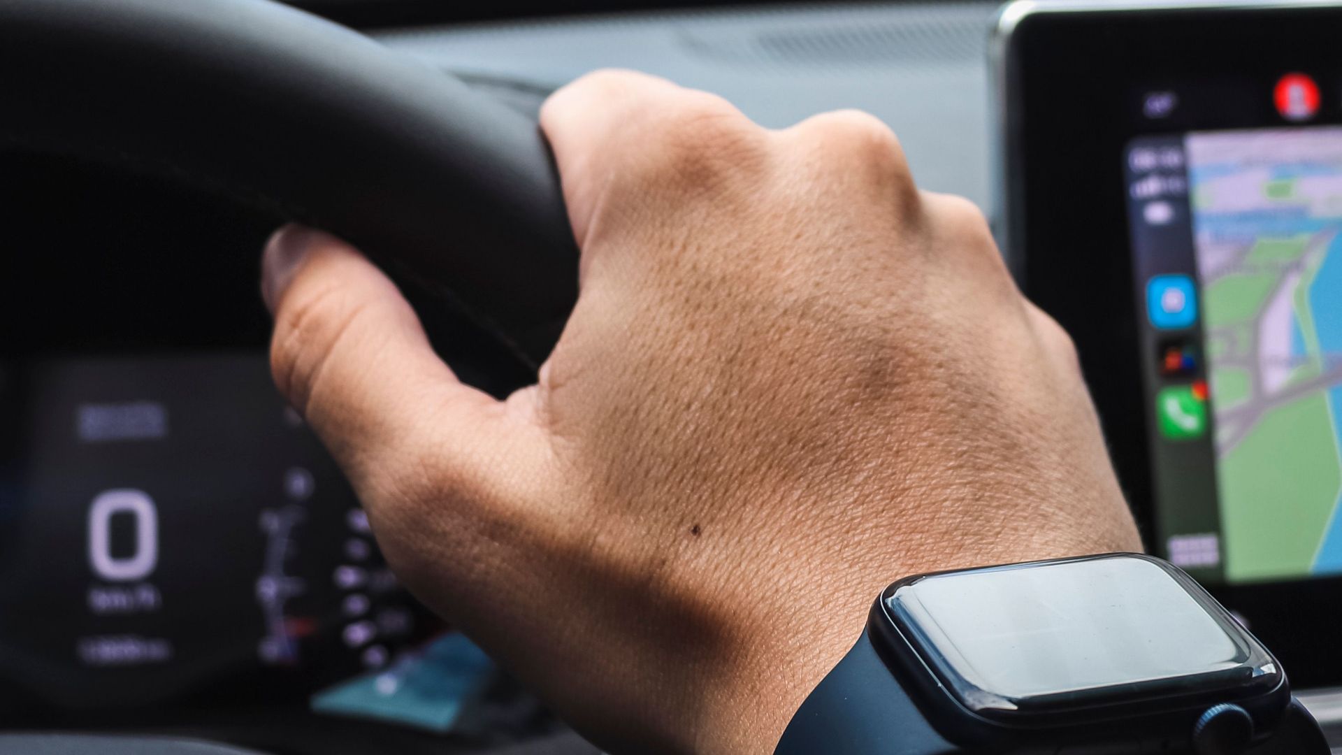 Close-up of a hand wearing a smartwatch while driving in a city setting.