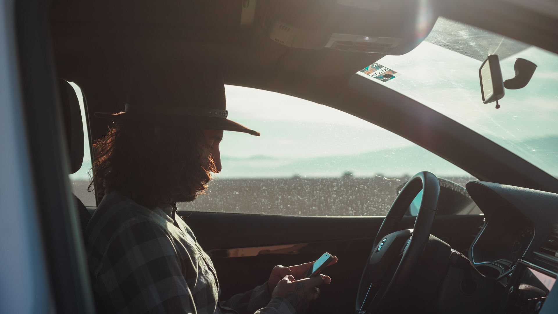 Profile of a man with a hat using a phone inside a car during the day.