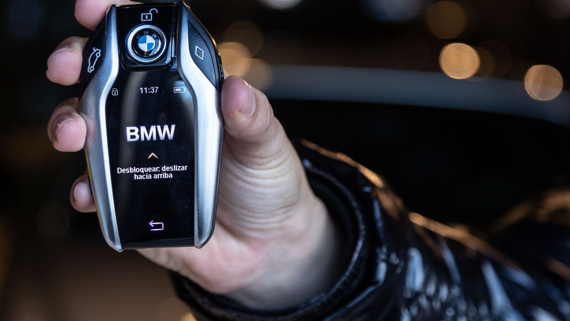 A close-up of a human hand holding a sleek black car key fob indoors.