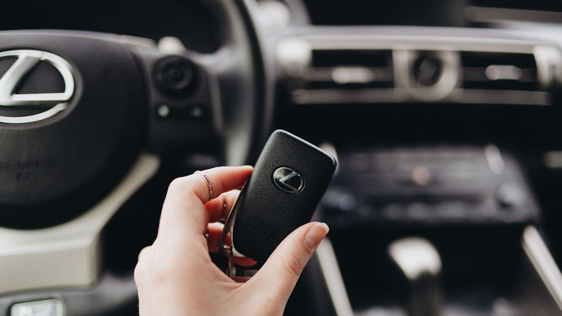 Person holding a Lexus car key inside a luxury vehicle's interior, showcasing brand elegance.