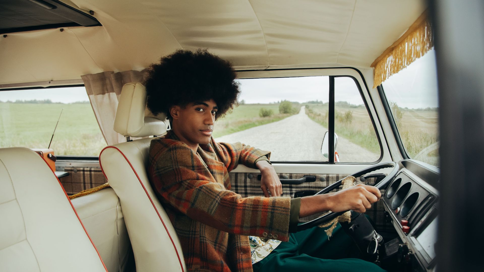A young man with an afro enjoying a scenic road trip in a retro van, exuding vintage style and wanderlust.