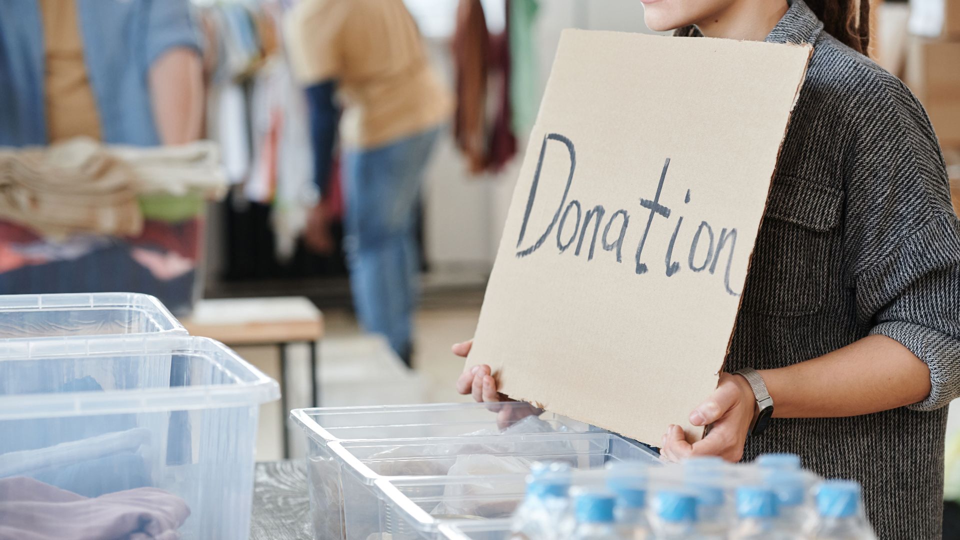 A volunteer holds a cardboard donation sign at a charity event with donation boxes ready for collection.