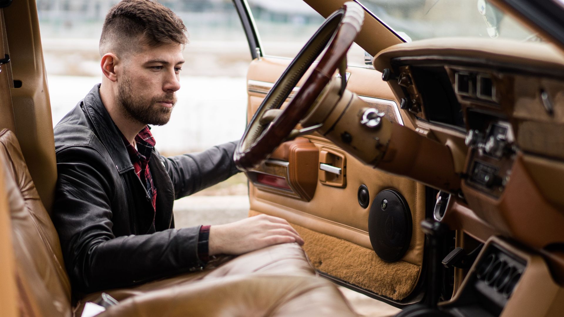 Confident adult man in leather jacket and shirt getting on driver seat of car on street in daylight