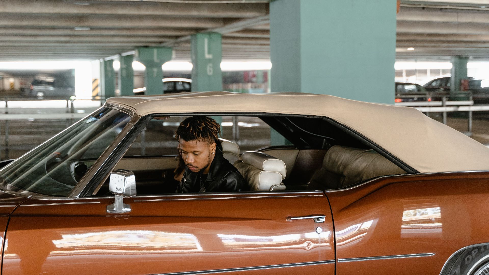 Man sitting in a classic convertible inside a parking garage.