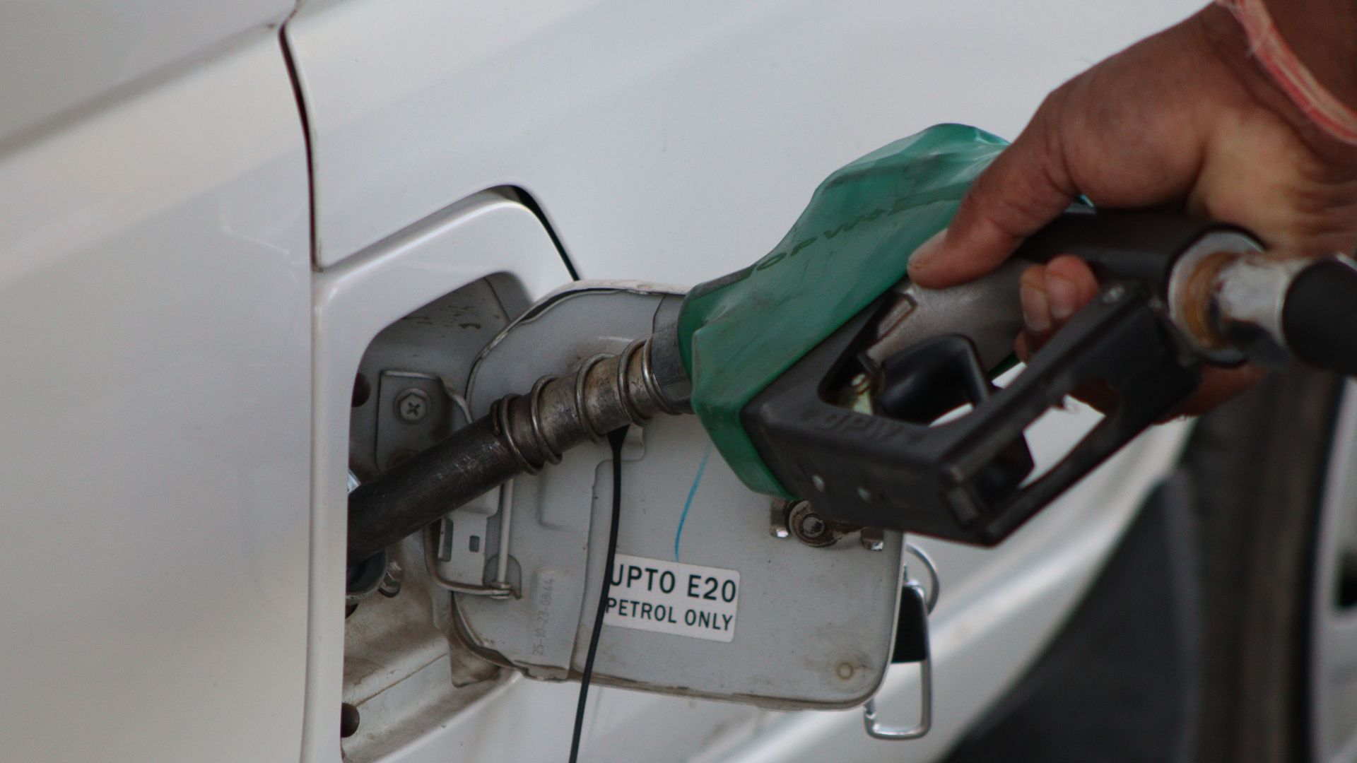 Hand refueling car with E20 petrol at a gas station, close-up view.