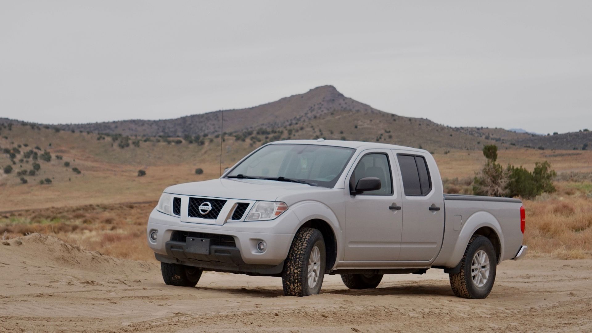 Silver pick-up truck parked on a rural dirt road in a rugged countryside landscape.