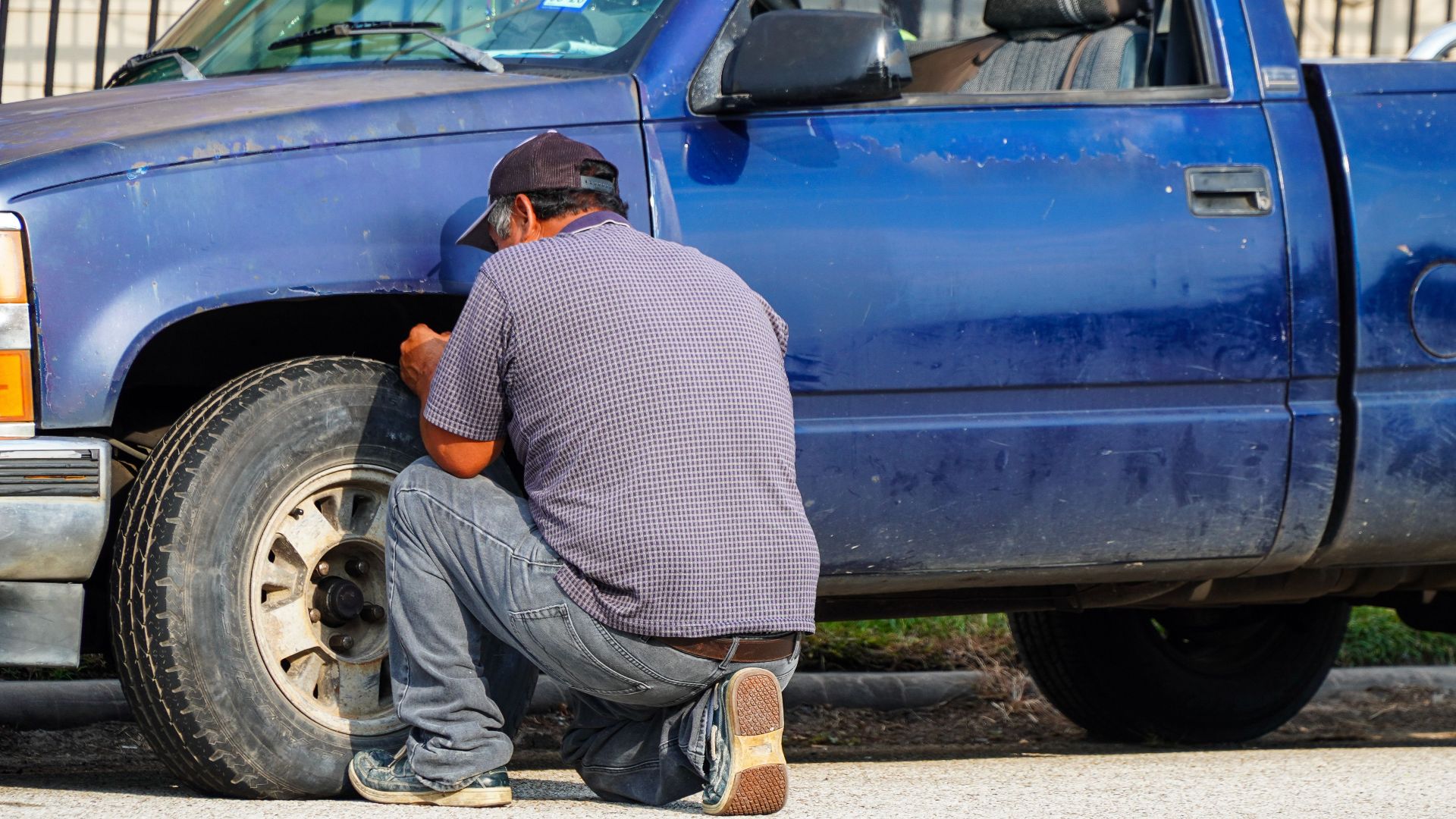 A man attentively repairing a flat tire on a blue truck in sunny Houston, Texas.