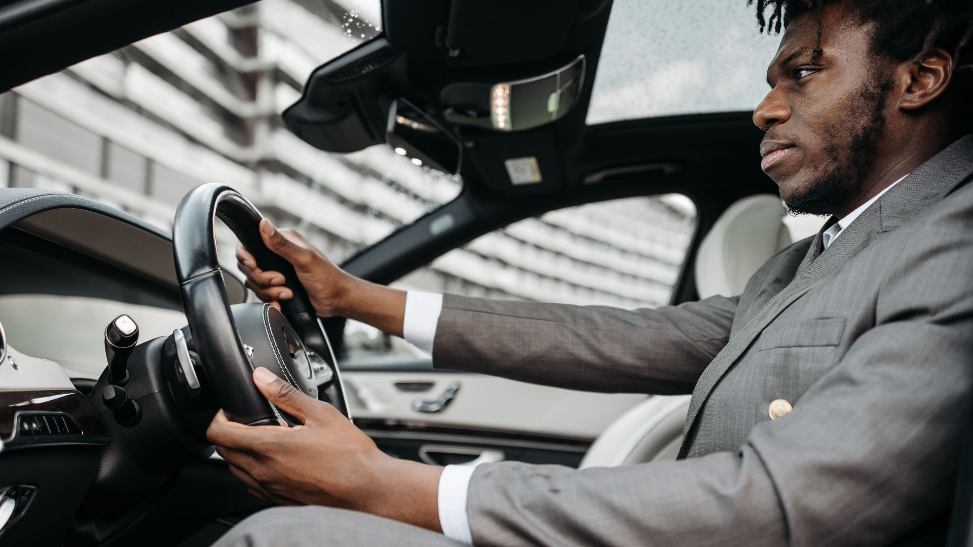 Man in a gray suit driving a luxury car, focused on the road.
