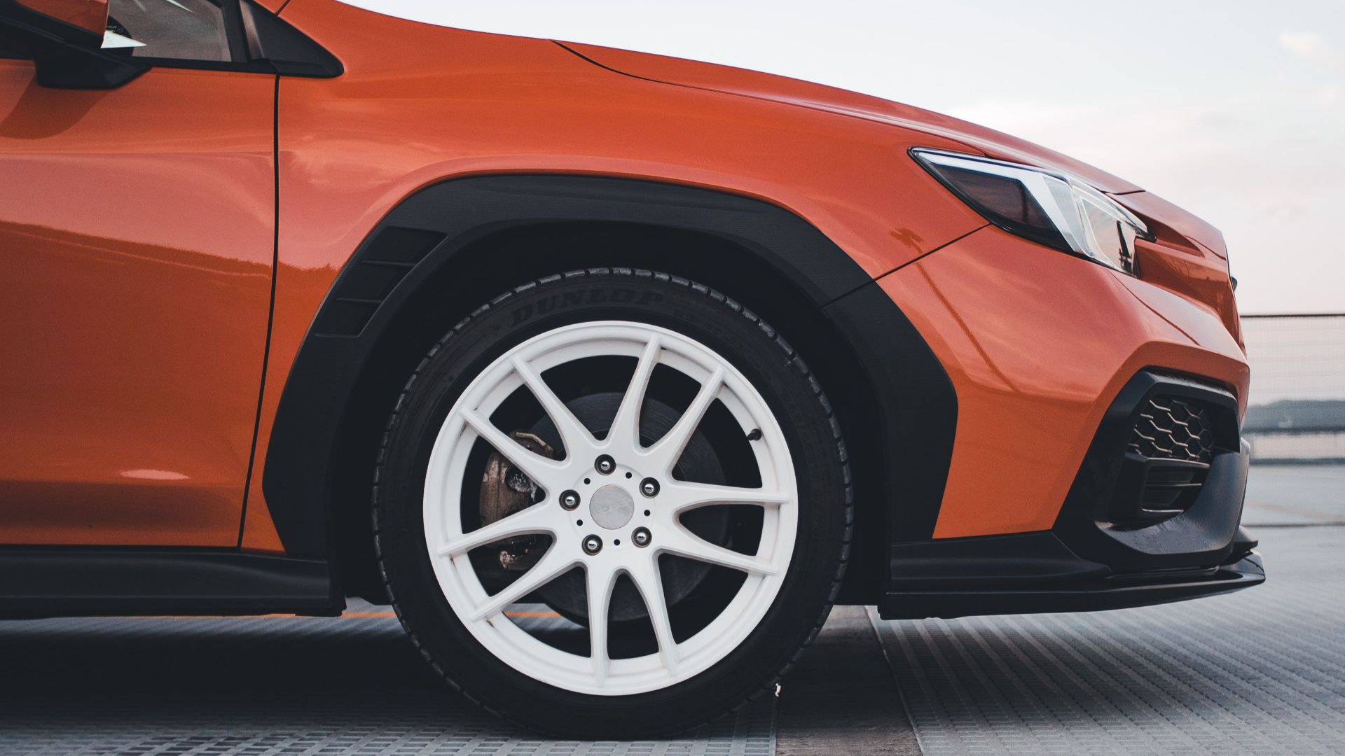 Side view of an orange sports car parked on a rooftop with a modern urban background.