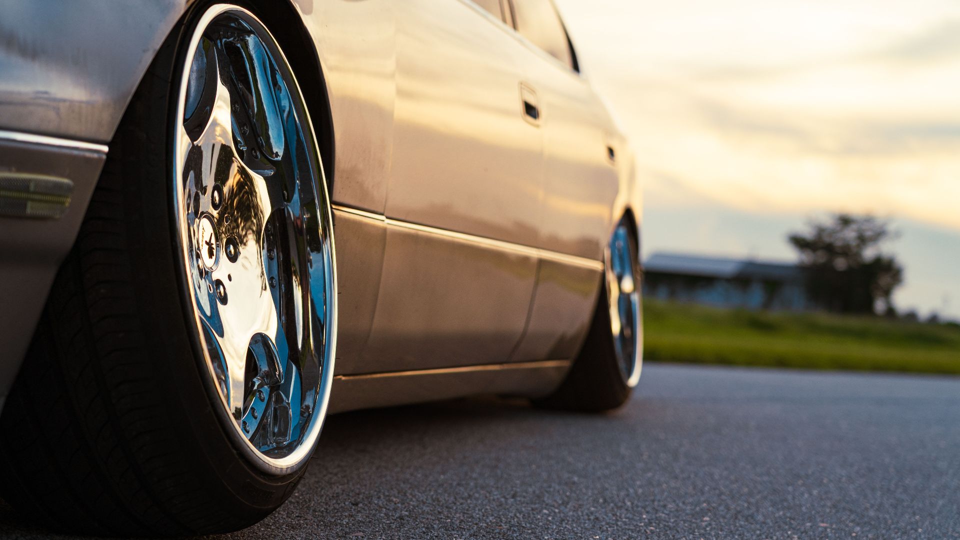 A stylish car parked on the road with reflective chrome wheels gleaming at sunset.