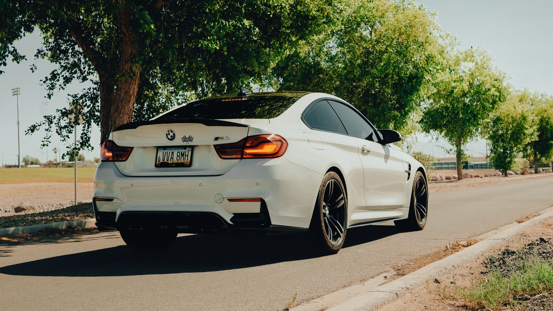 A sleek white luxury car on a scenic road bathed in sunlight, flanked by green trees.