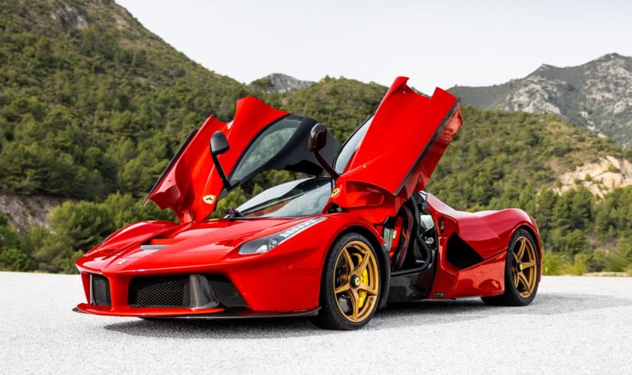 A striking red sports car with open doors against a serene mountain backdrop