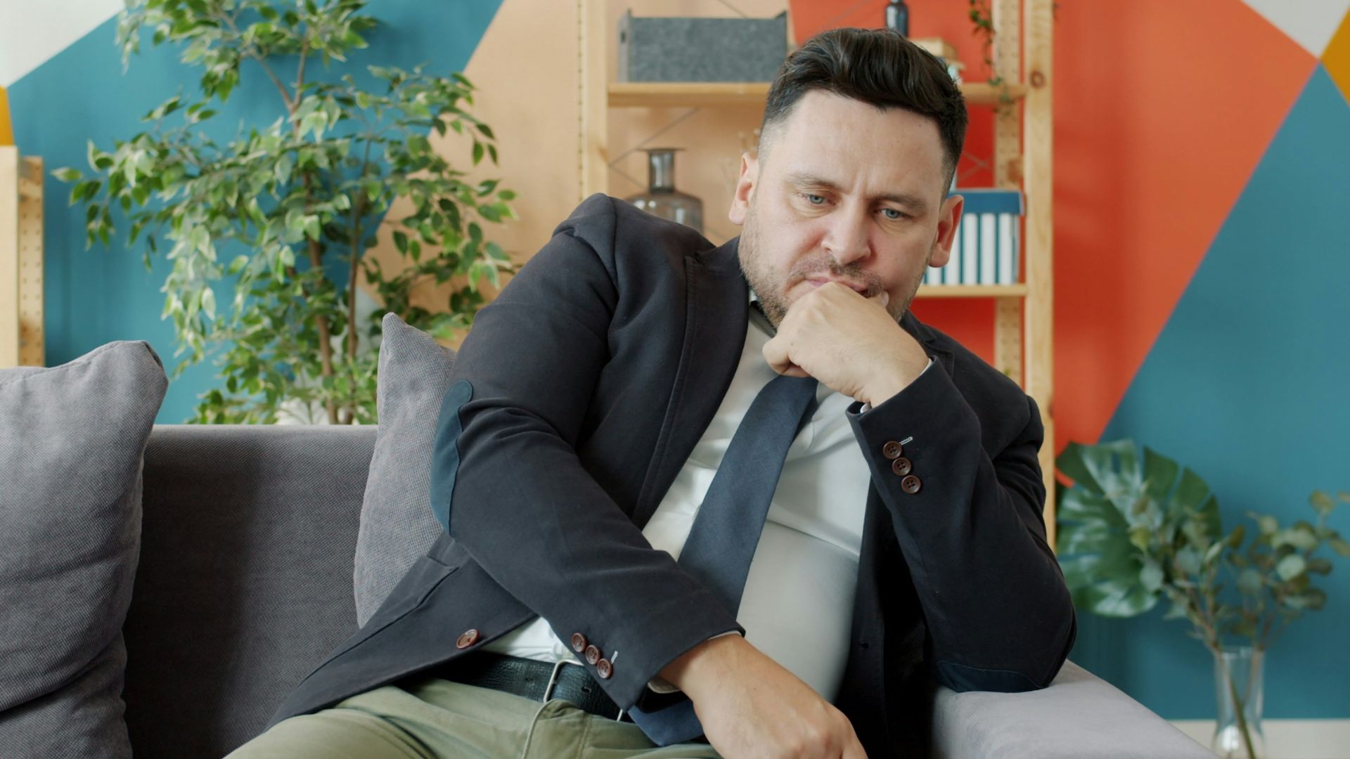 Man in suit sitting on couch looking thoughtful.