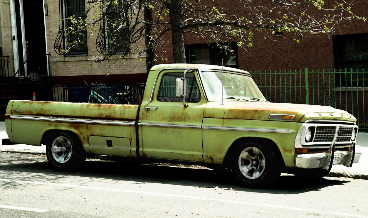 Rusty green vintage pickup truck parked on a city street