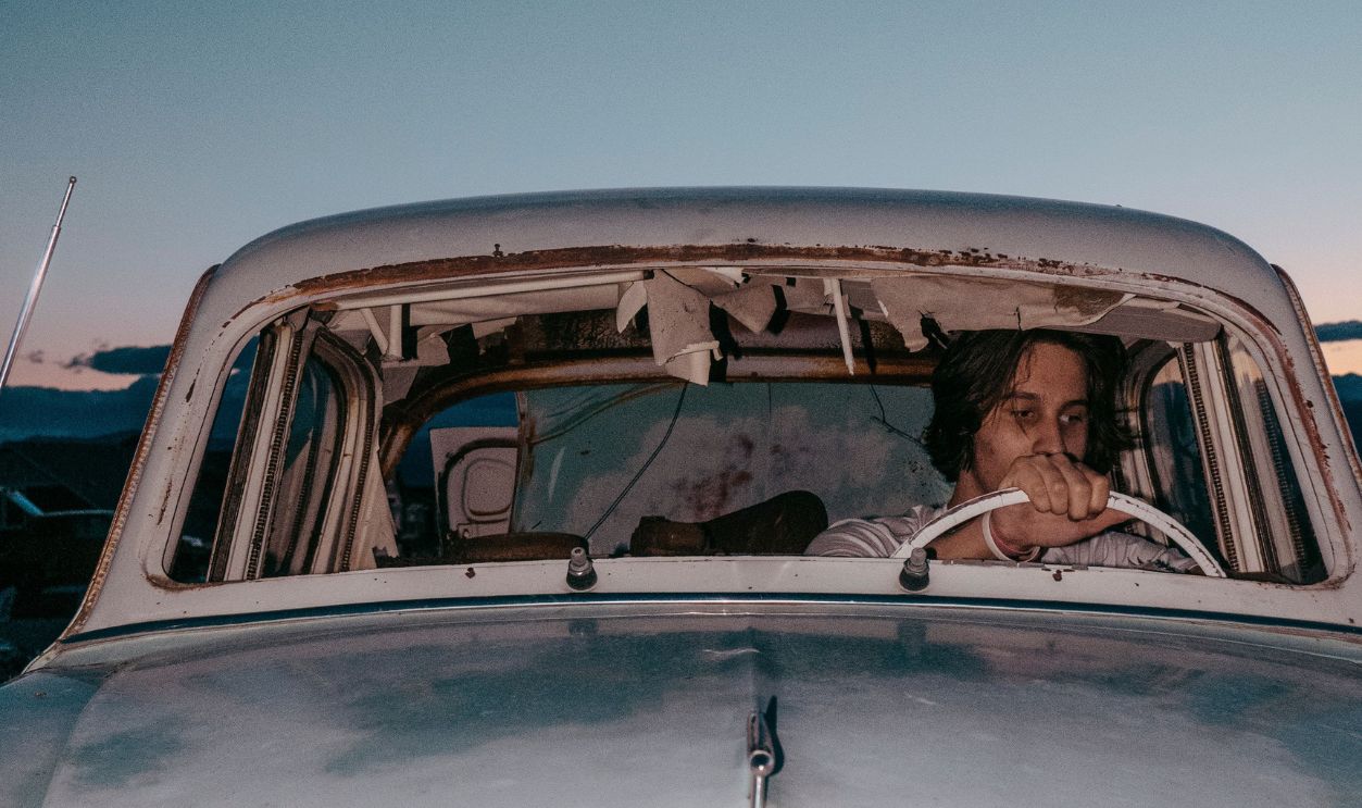 A man sitting in a vintage car during twilight, evoking nostalgia