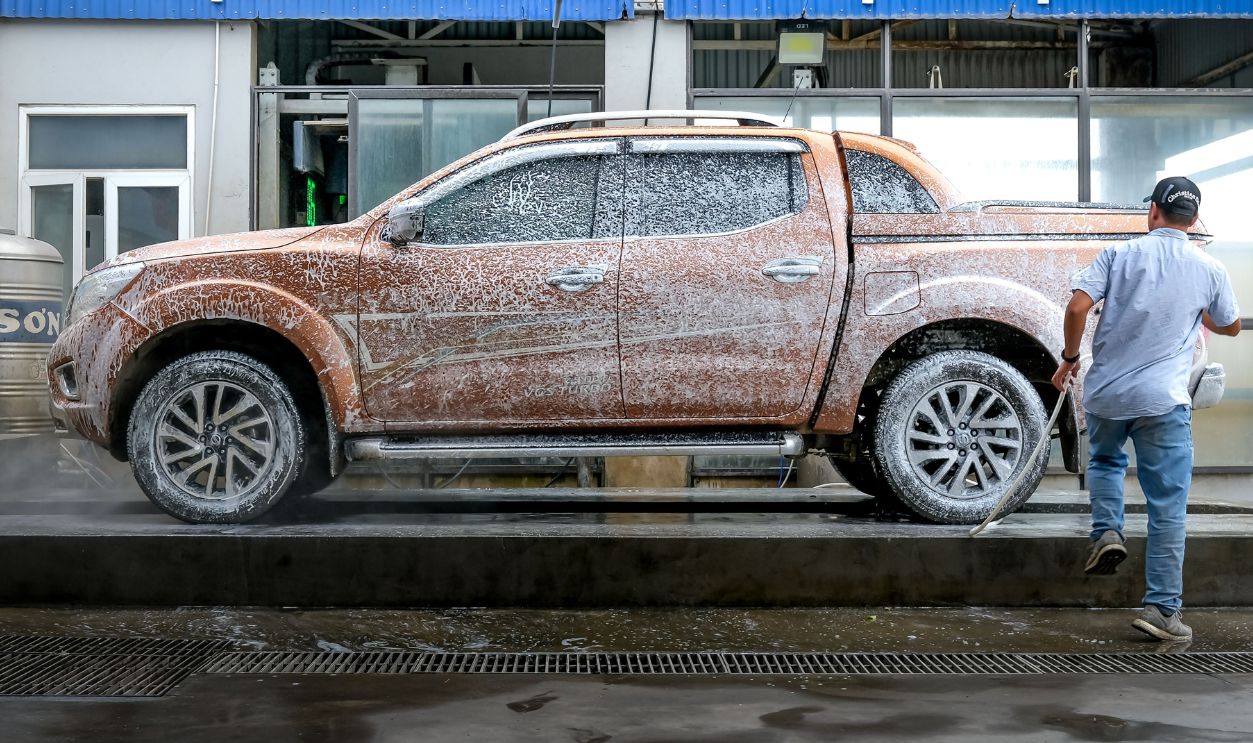 A man cleans a foamy pickup truck at an automatic car wash station