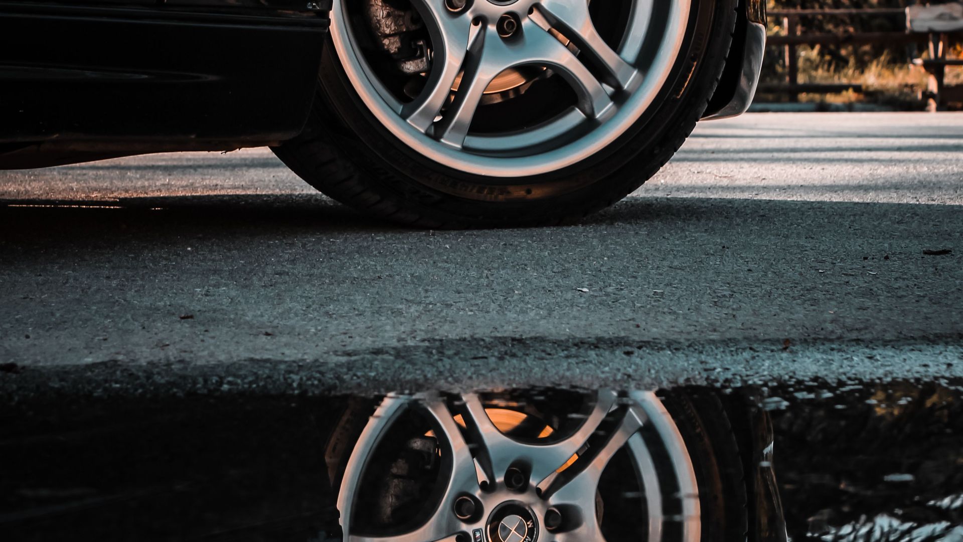 A stylish black car's wheel reflected in a puddle on a street in Türkiye.
