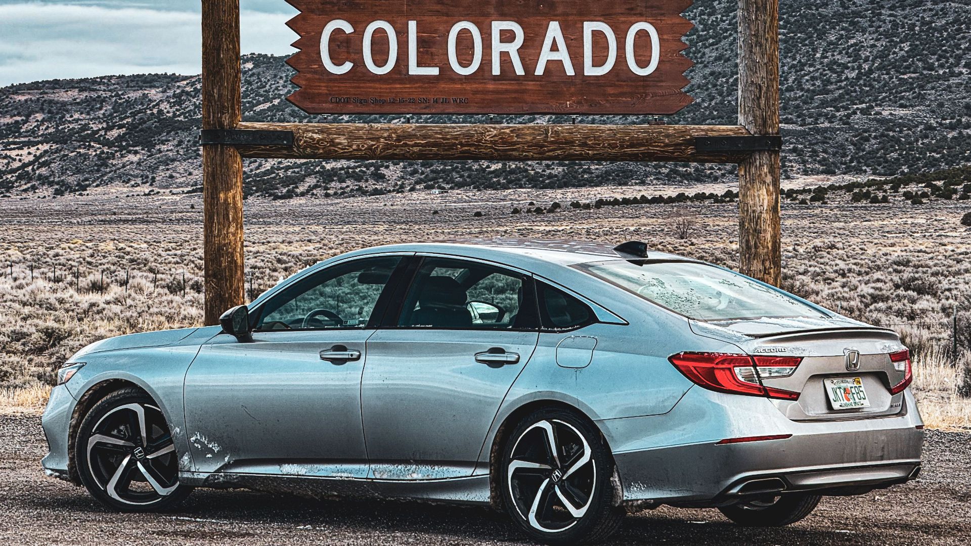 A silver sedan parked by a scenic Welcome to Colorful Colorado sign on a cloudy day.