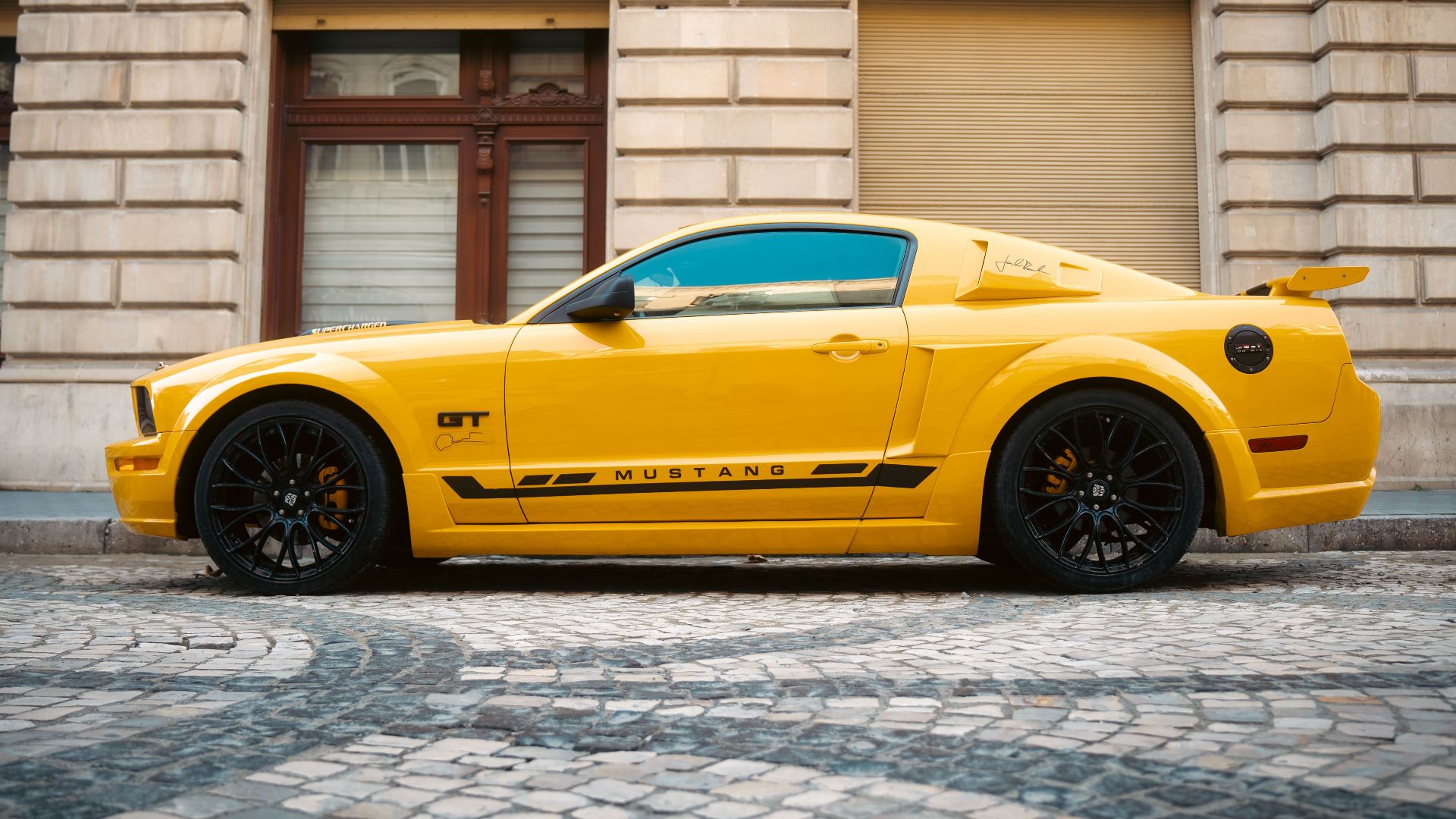 Vibrant yellow Ford Mustang sports car parked by a historic building in Baku, Azerbaijan.