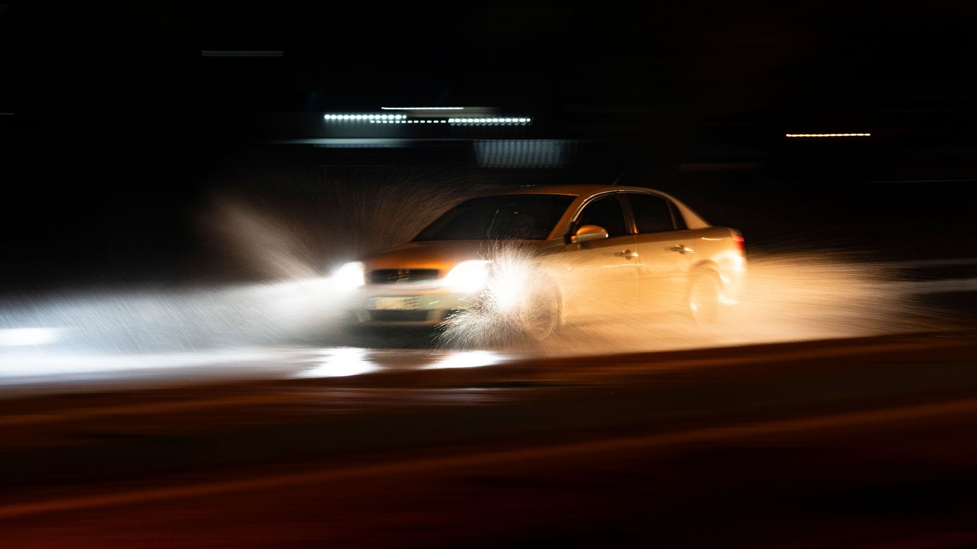 A car speeding through a wet road with dramatic splashes during a nighttime drive.