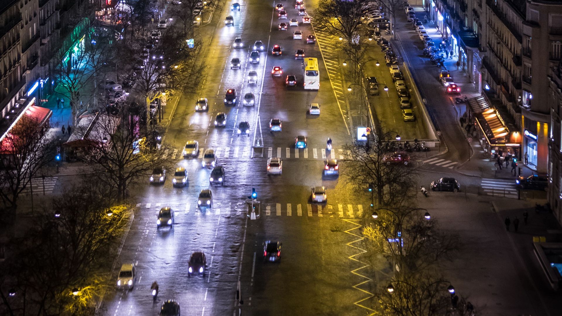 Aerial view of a vibrant Paris street at night, showcasing city lights and bustling traffic.