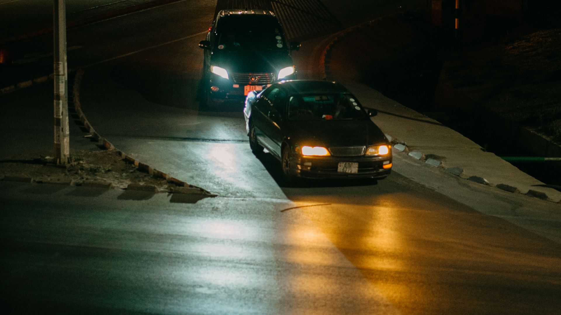 A dimly lit urban street at night featuring cars and street lights creating a dramatic cityscape.