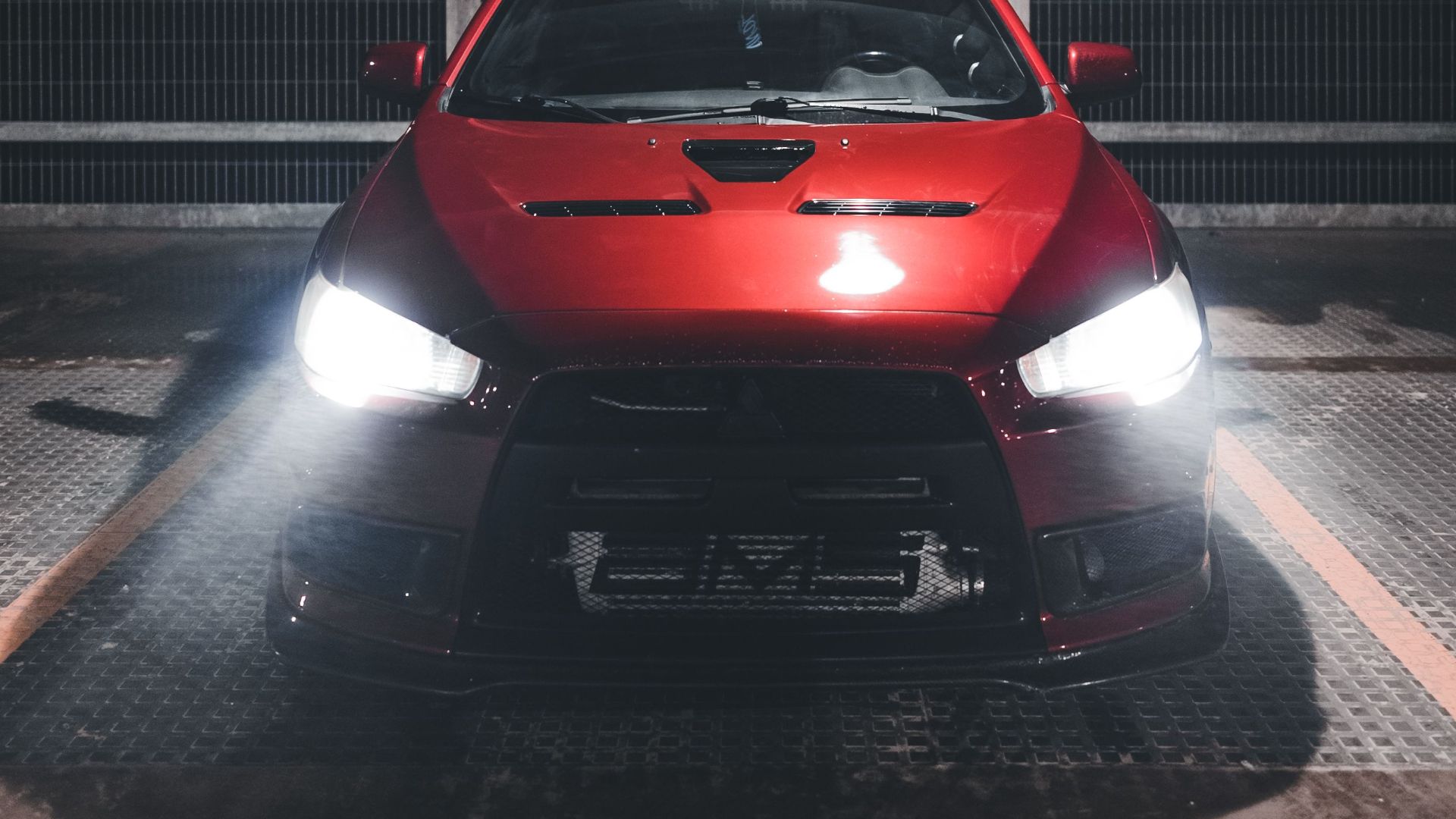 Front view of a red car with headlights on in a parking lot at night.