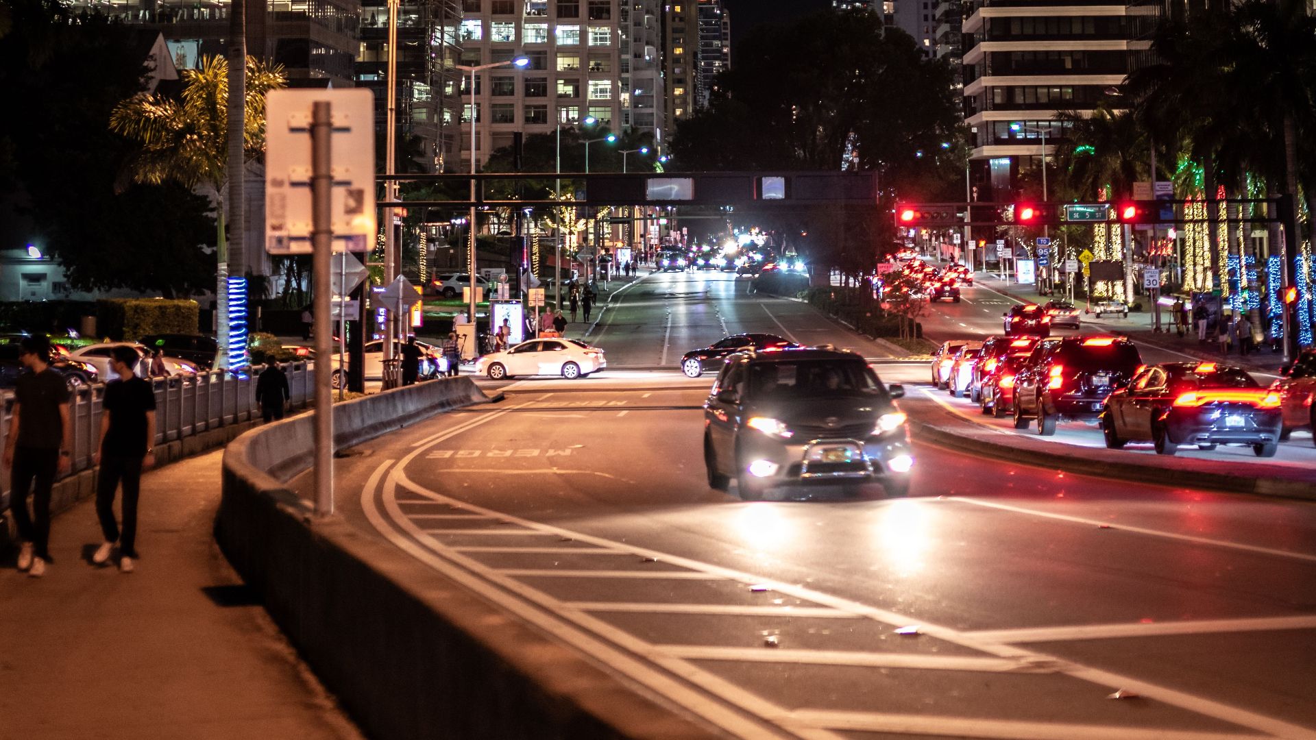 A lively nighttime scene in downtown Miami with illuminated skyscrapers and bustling traffic.