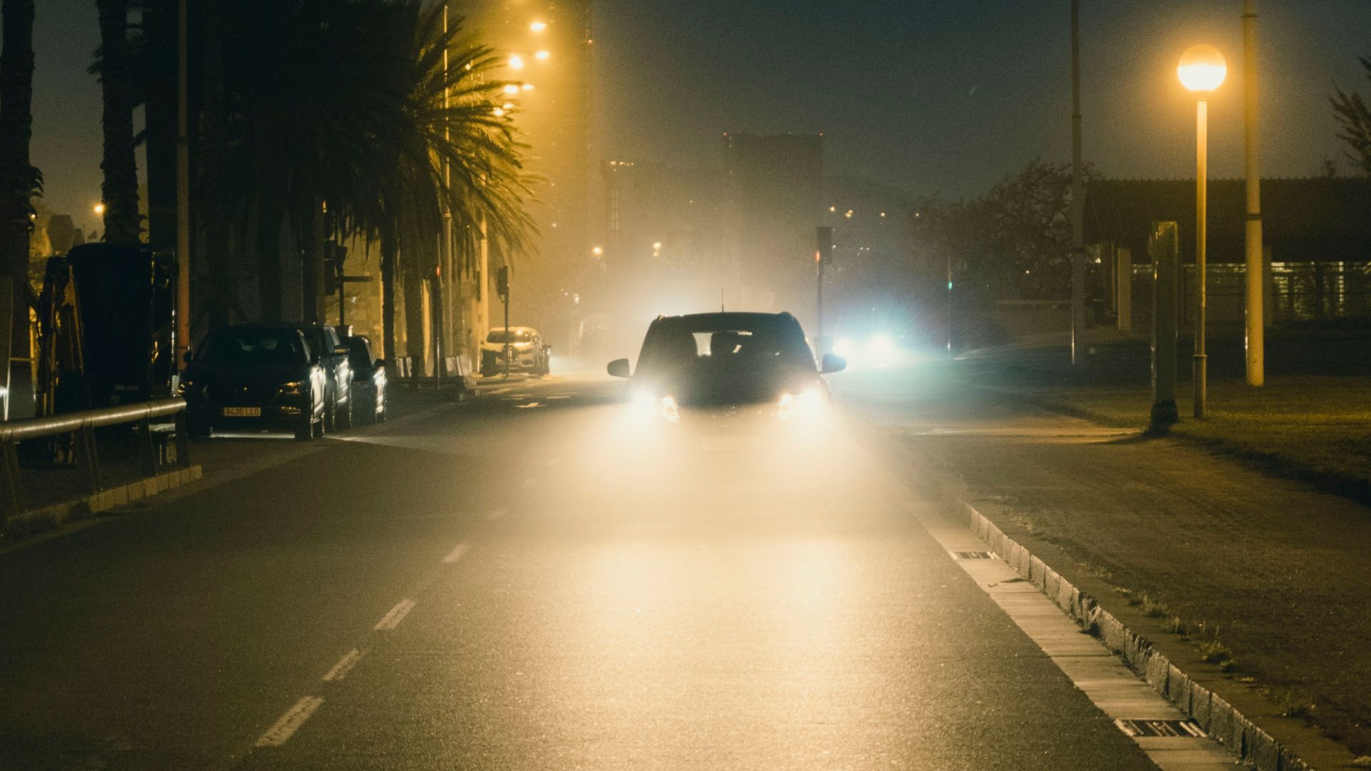 Mysterious night cityscape with a car driving down a street, illuminated by headlights.