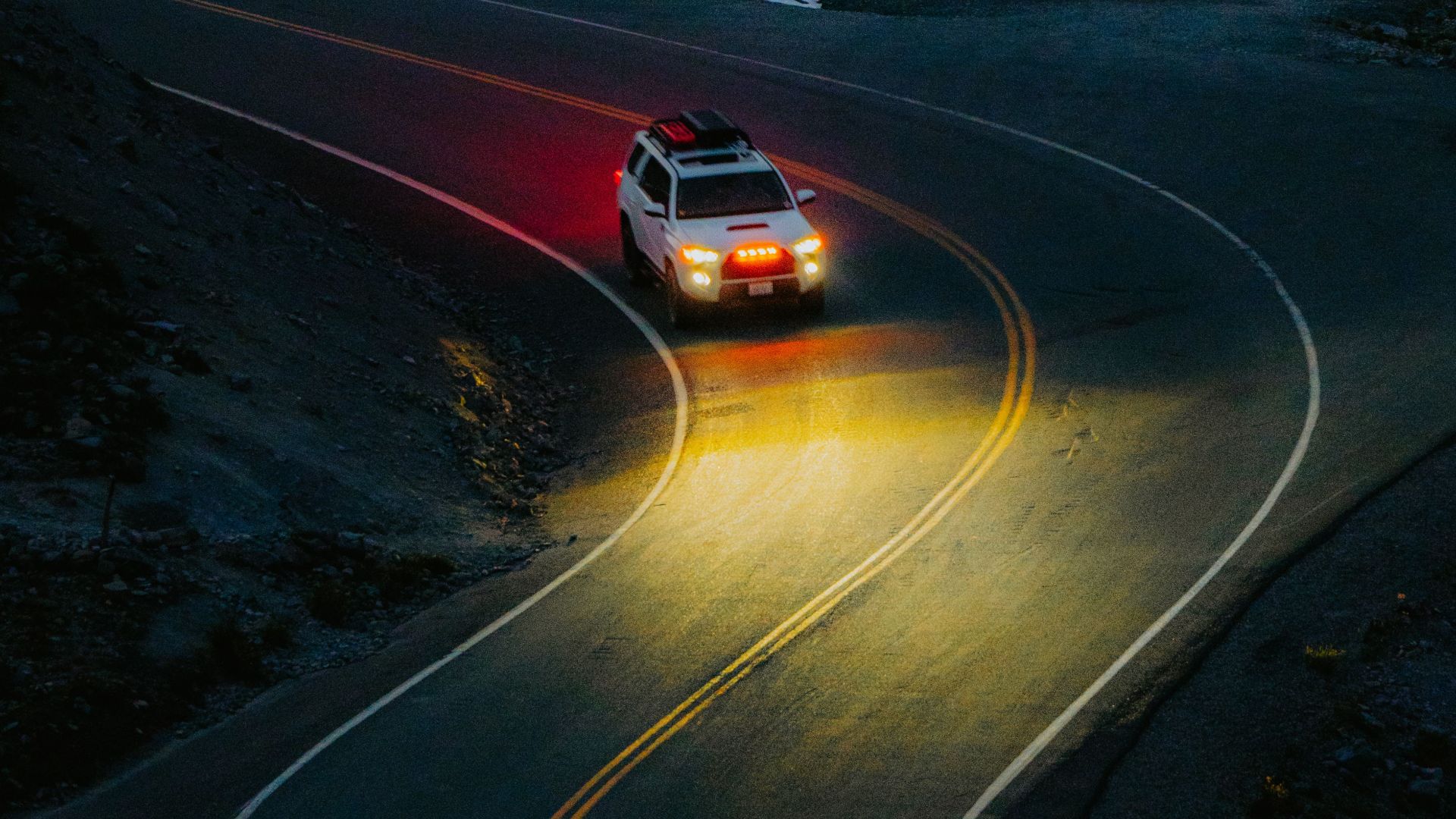 A white SUV navigating a winding mountain road under dark, atmospheric lighting.