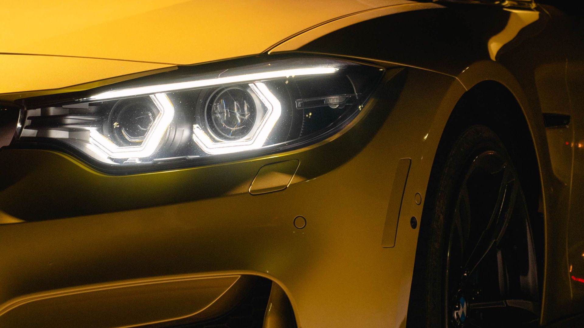 Close-up of a shiny yellow luxury convertible car with bright LED headlights against a dark background.