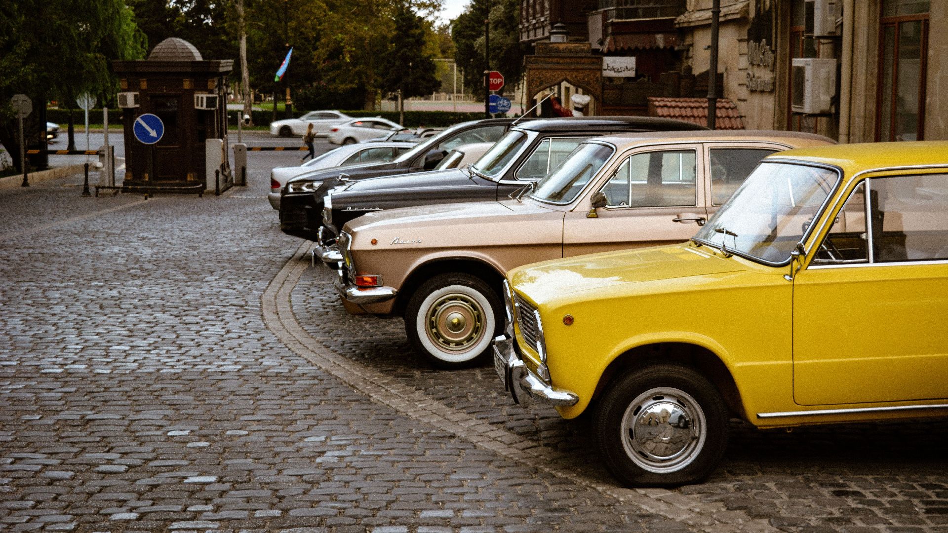 A row of colorful classic vintage cars parked on a cobbled street in a historic area.