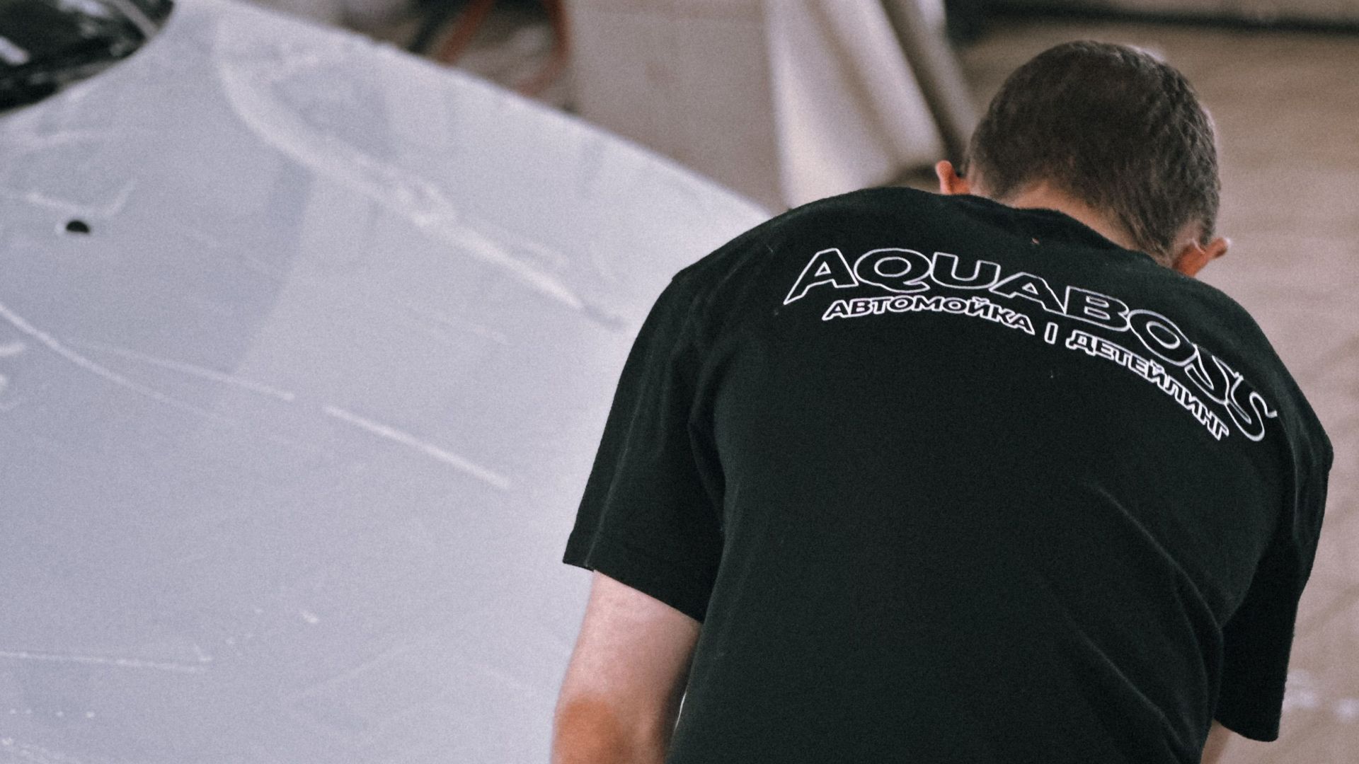 Professional cleaning a white car with foam in an auto garage.