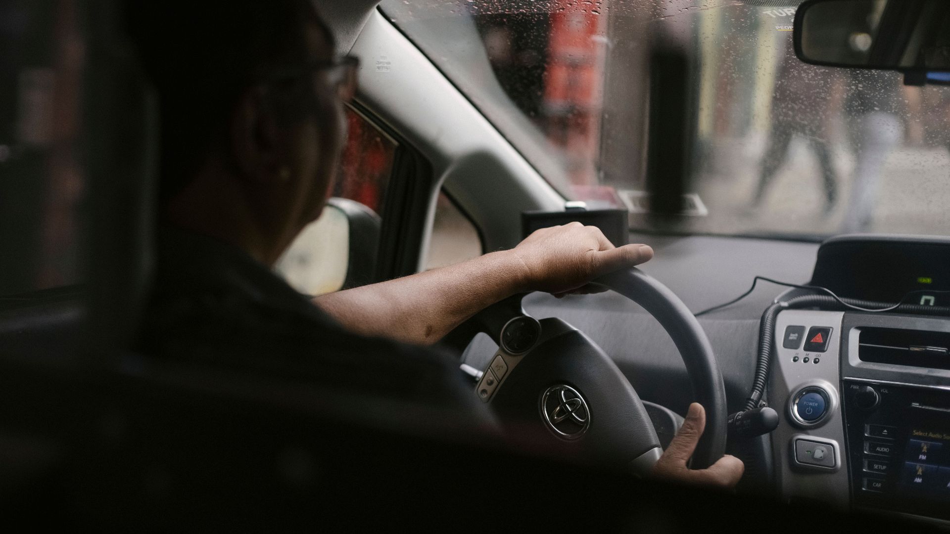 Back view of crop anonymous man in eyeglasses driving car in rainy day