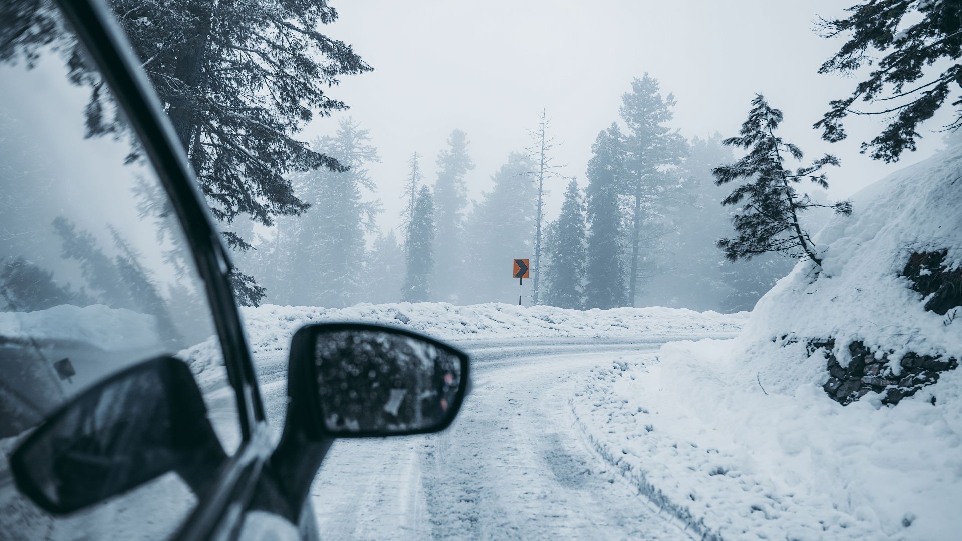 A car drives through a foggy snow-covered mountain road, capturing winter's serene beauty.