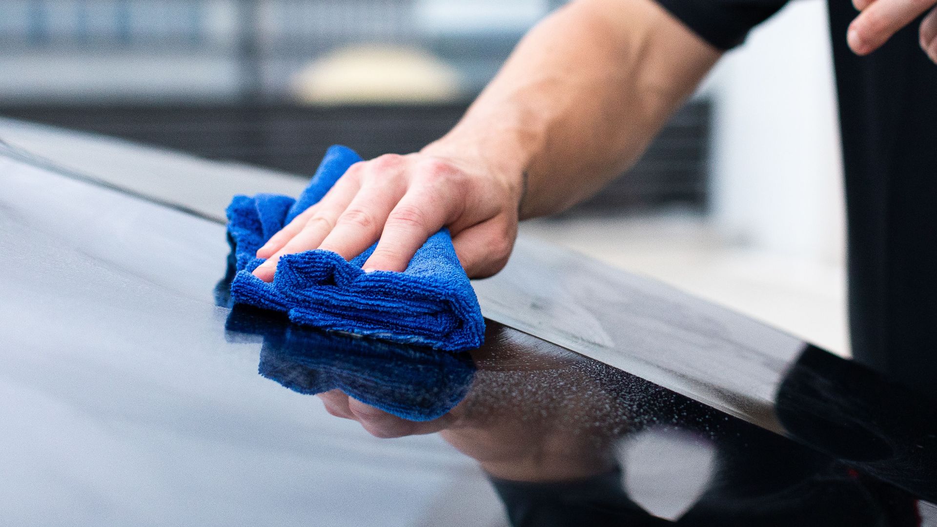 Hands cleaning car with microfiber cloth and spray cleaner for a shiny finish.