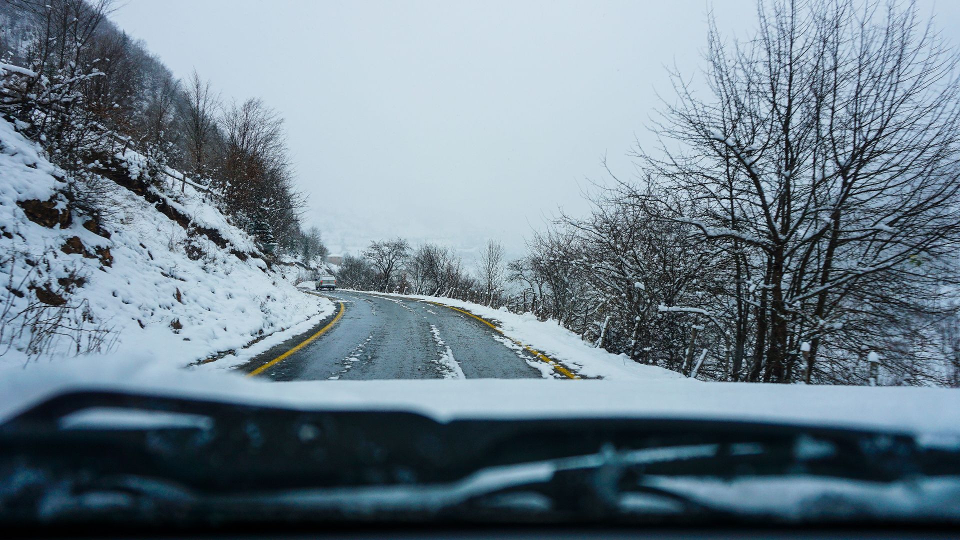 A scenic winter road view through snow-covered trees and hills.