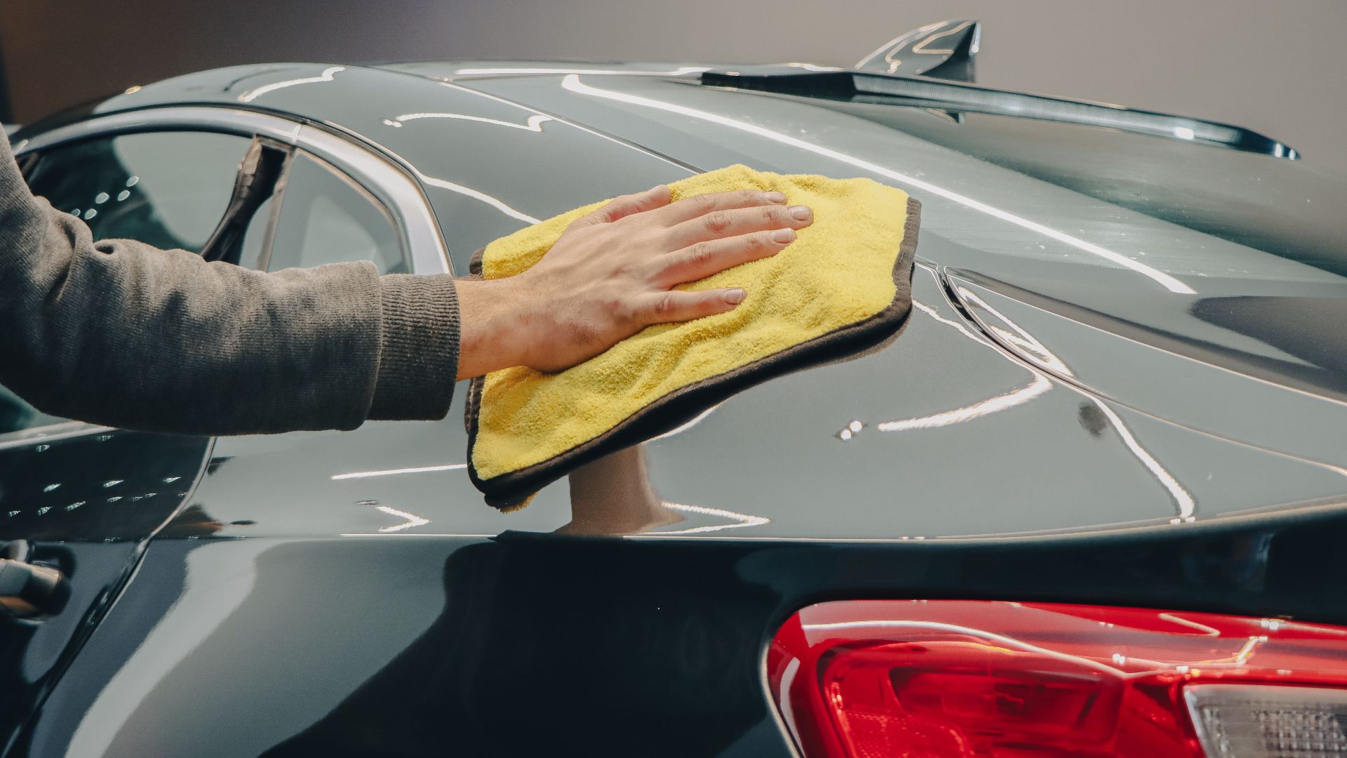 Close-up of hand polishing a shiny car with a yellow cloth indoors.