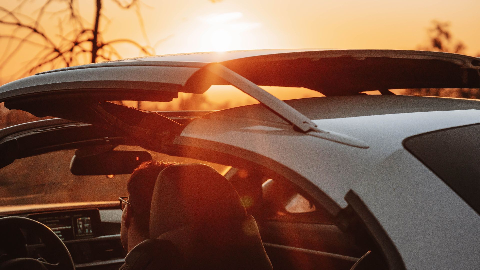 Person in convertible car driving during sunset with sun glare creating a warm atmosphere.