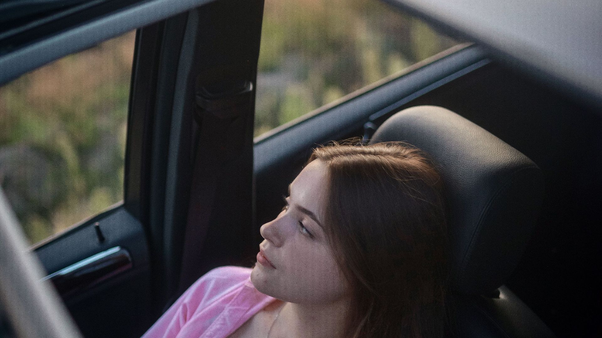 A young woman in a car with an open sunroof, enjoying a serene outdoor view.