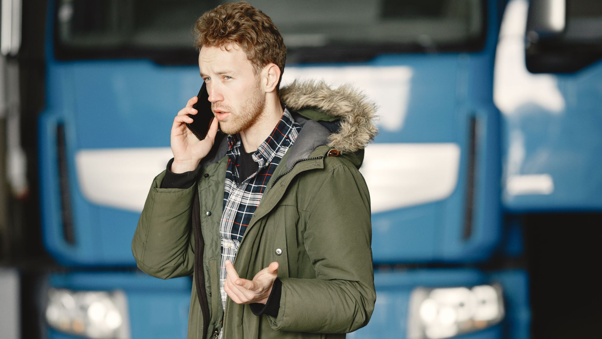 Man in a green parka talking on the phone in front of a blue truck.