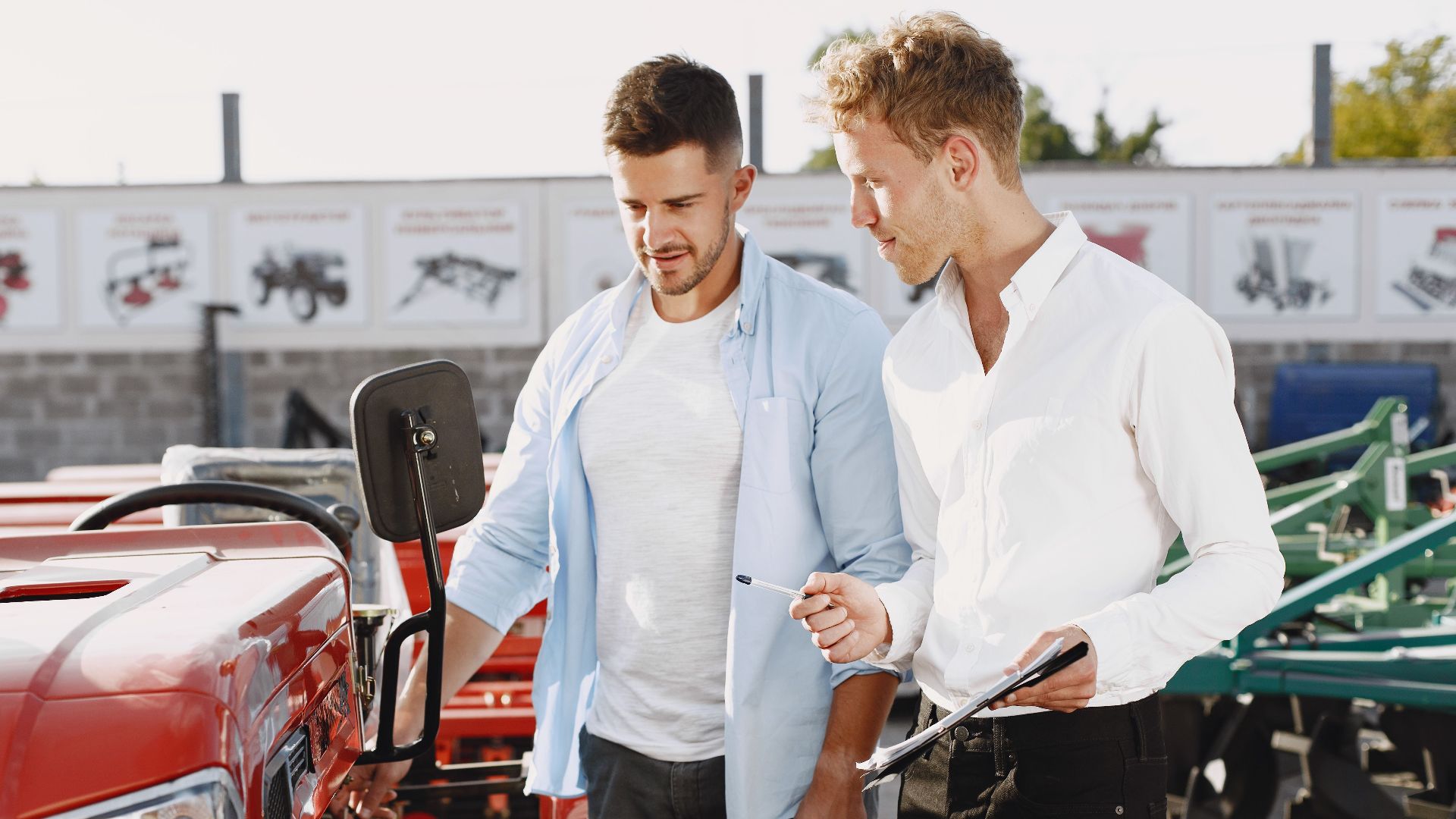 Two men having a discussion about a red tractor in an outdoor setting, possibly negotiating a deal.