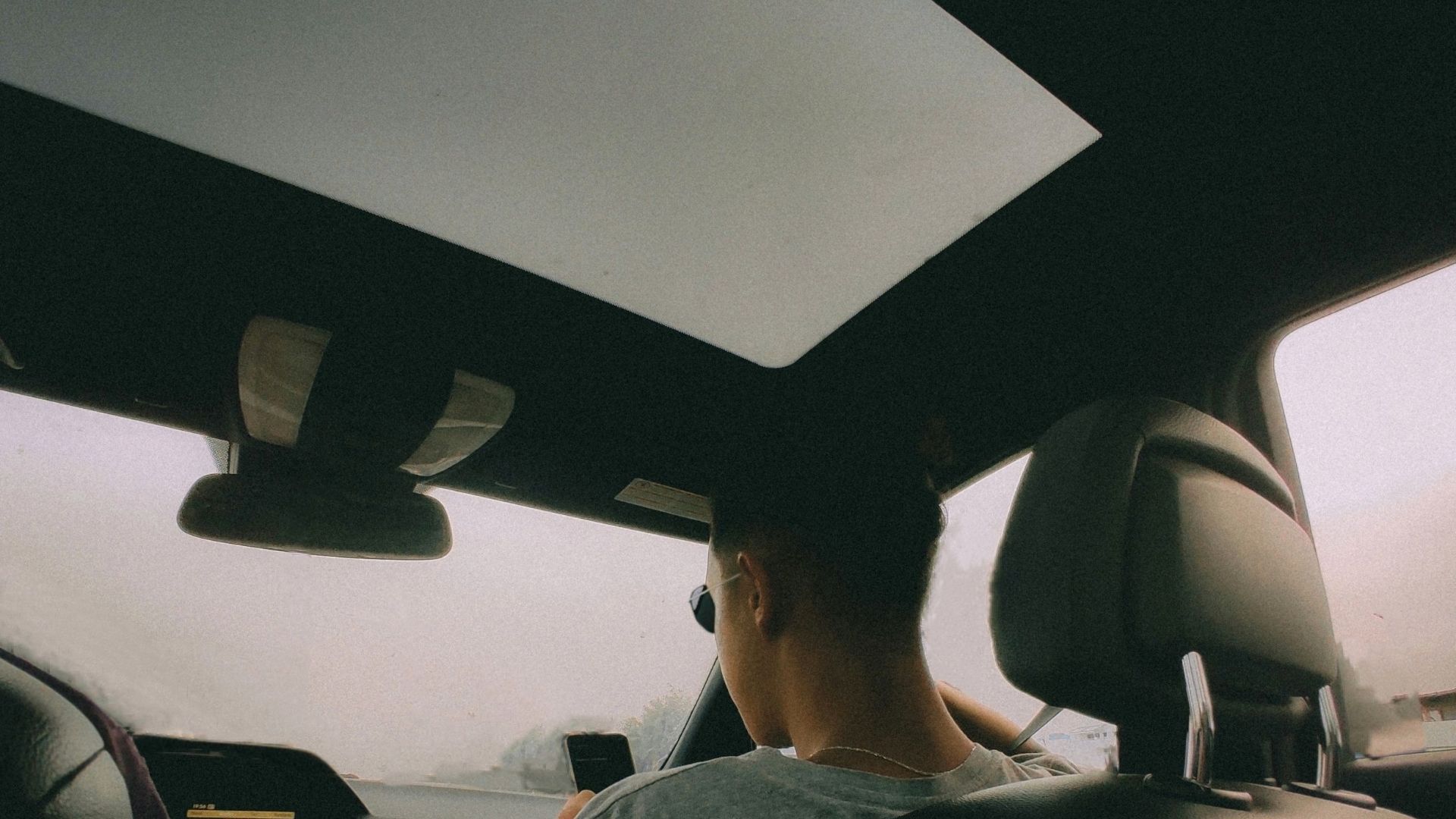 Back seat view of two people driving in a car on a cloudy day.