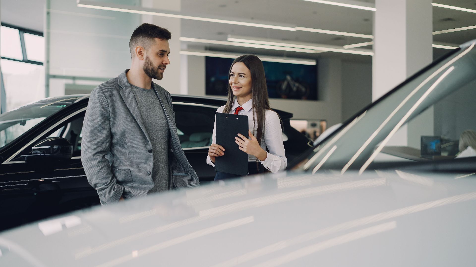 Man consults with salesperson in modern car dealership showroom.