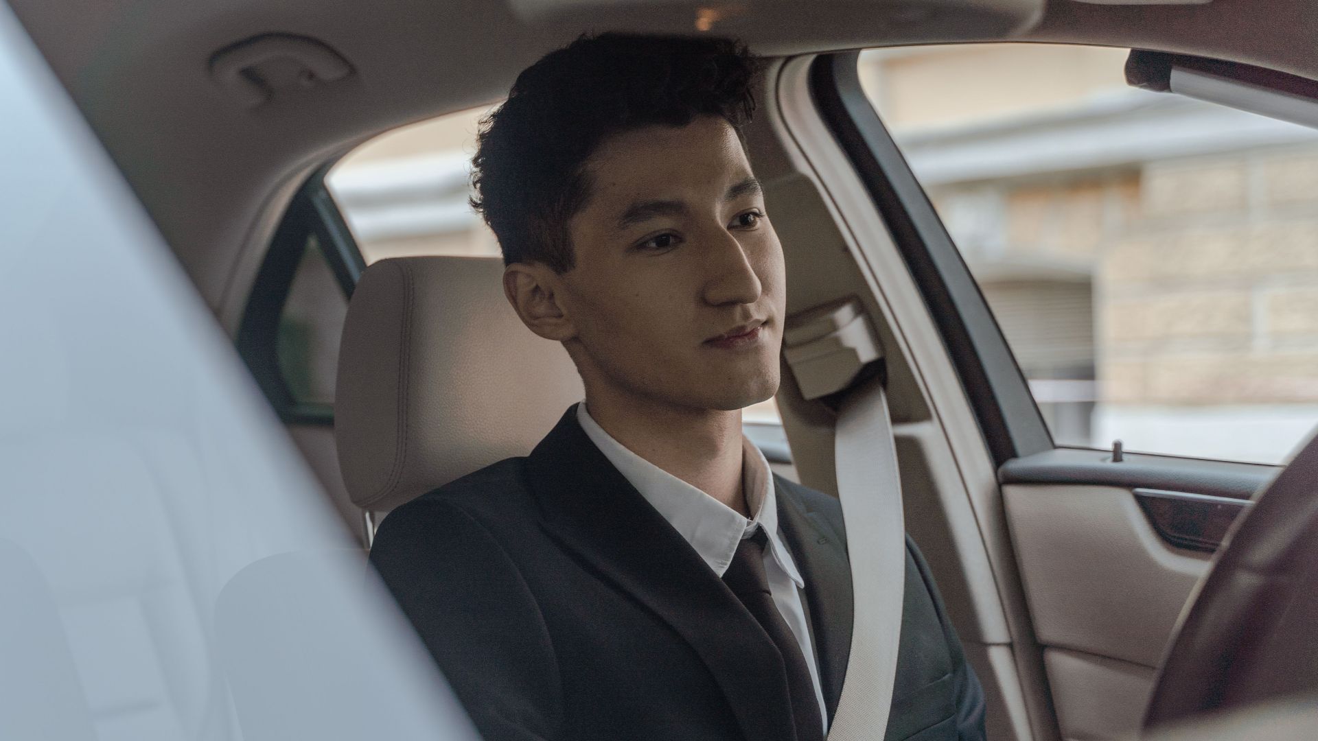 Young professional driver in formalwear inside a modern car, looking focused and attentive.