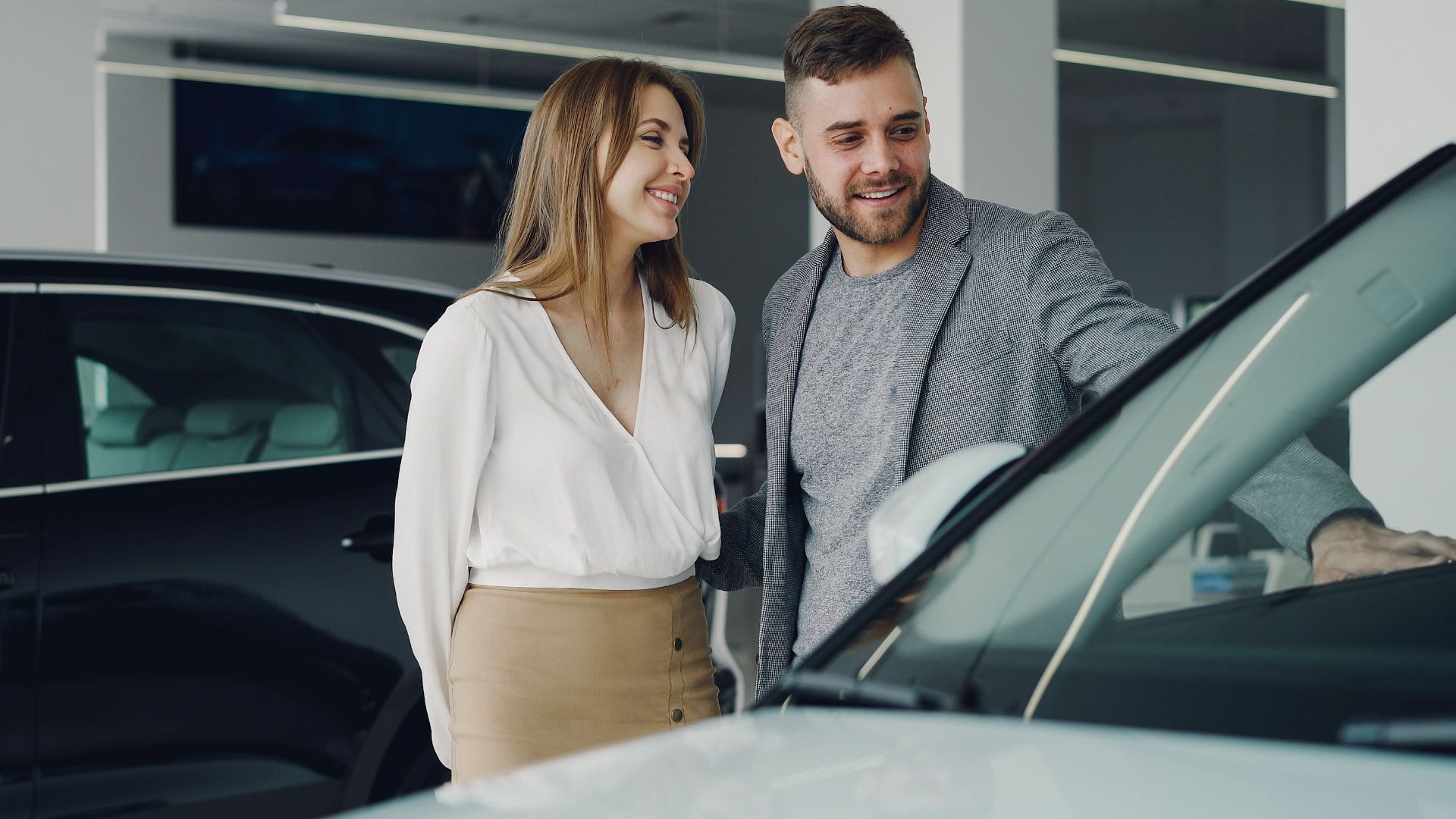 Smiling couple exploring cars at dealership, enjoying shopping experience.