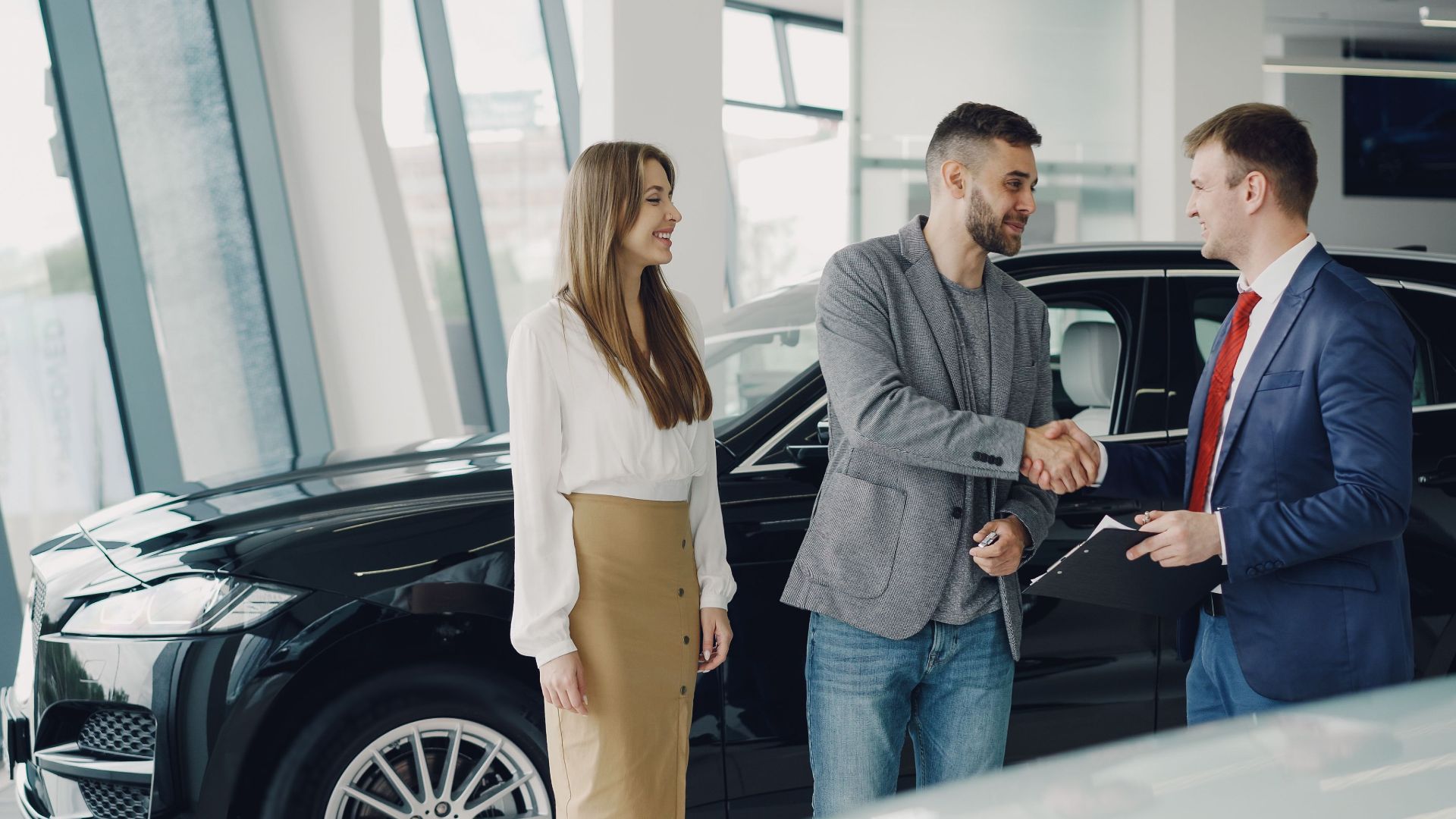 Customers shaking hands with dealer in showroom, sealing car purchase deal.