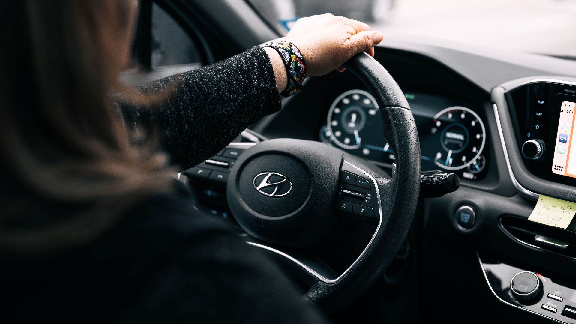 A woman driving a Hyundai car, focusing on the steering wheel and dashboard controls.